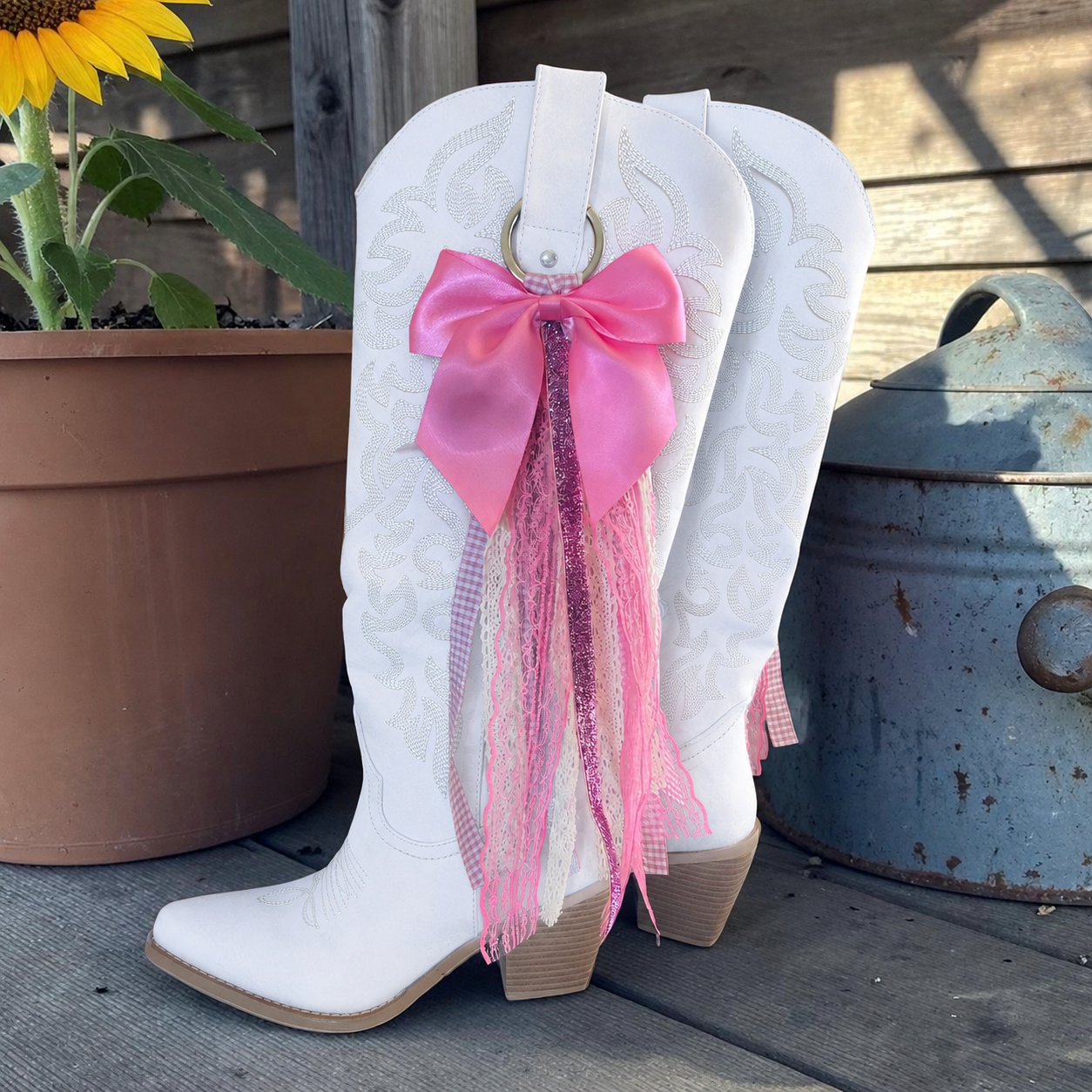 White cowboy boot with a pink bow and tassels on a wooden surface.