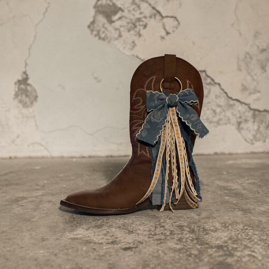 Brown cowboy boot with decorative bow and lace on a textured surface